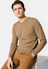 Brązowy sweter z dekoltem w serek z miękkiej dzianiny, z prążkowanymi mankietami i dołem, w zestawie z beżowymi spodniami slim-fit. Dyskretne logo na piersi.