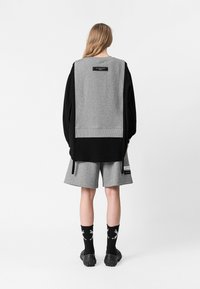 Sudadera en gris y negro, con mangas largas y un dobladillo acanalado. Combinada con pantalones cortos grises y calcetines negros con un diseño blanco.