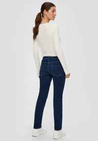 Jean bleu marine avec taille haute et coupe slim, dotés de poches arrière et d'une texture en denim lisse, associés à un haut à manches longues en côte blanc.