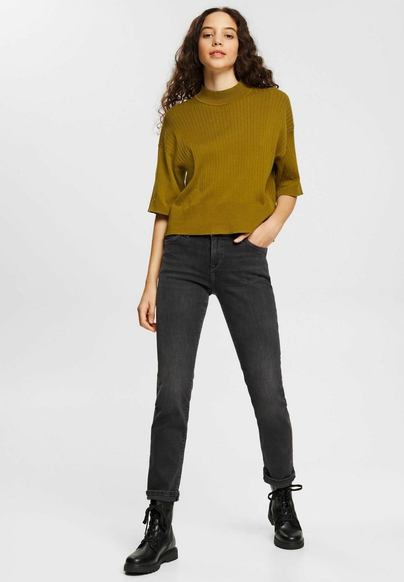 Haut en tricot côtelé moutarde à manches courtes, associé à un jean noir slim et des bottines à lacets noires. Design simple, look décontracté.