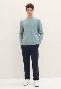 Lichtblauwe gebreide trui, ronde halslijn; marineblauwe broek; witte sneakers; relaxte pasvorm, zichtbare textuur in de stof en een gladde afwerking op de schoenen.