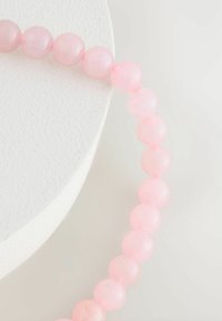 Rose quartz bead necklace with smooth, round beads in varying shades of pink. Placed on a textured white circular surface.