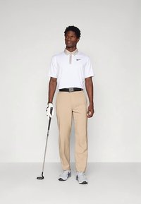 Vit pikétröja med beige detaljer, beige byxor och grå golfskor; håller en golfklubba; enkel design, inga mönster eller dekorationer.