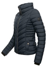 Donkerblauwe pufferjack met een chevron-quiltpatroon, opstaande kraag, ritssluiting en gebreide manchetten; heeft een logopatch op de mouw.