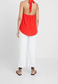 Rode mouwloze top met een halternekstrik, met een loose fit. Gecombineerd met witte cropped broek en zwarte sandalen met bandjes.