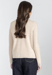 Beżowy sweter z długimi rękawami, prążkowanymi mankietami i dołem, wykonany z miękkiego materiału. Widok z tyłu pokazuje gładką fakturę i dopasowany krój.