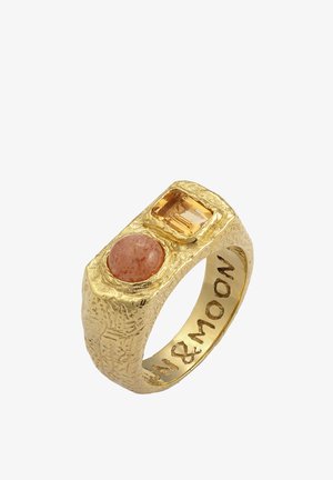 Zelta tonis gredzens ar teksturētu virsmu, kurā ir apaļa persiku krāsas akmens un taisnstūra dzeltenais kristāls. Izzīmēts ar uzrakstu "Saule un Mēness".