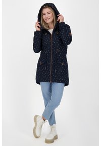 Giacca blu navy con pois, con cappuccio, chiusura con zip, due tasche frontali e dettagli in toggle, abbinata a jeans azzurri e stivali bianchi da combattimento.