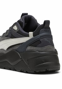 Dark gray sneaker featuring a padded collar, textured mesh, and white accents. Thick black sole with subtle branding detail on the heel.