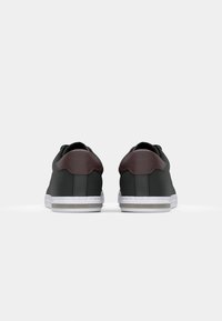 Zwarte sneakers met een donker bordeauxrode hielaccent, witte zool, een soepele textuur en een minimalistisch ontwerp. Bevat een logo op de buitenste hiel.