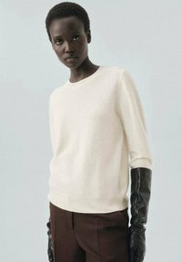 Pull crème avec un col rond et une coupe légèrement ample, associé à un pantalon marron taille haute et de longs gants en cuir noir.