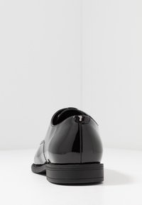 Chaussures en cuir verni noir avec une texture lisse, bout arrondi et une semelle noire en caoutchouc basse. Comprend des détails de couture minimalistes.