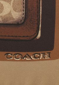 Acercamiento a una tela con un parche de cuero marrón que presenta bordes cosidos y la palabra "COACH" impresa debajo en letras gruesas.