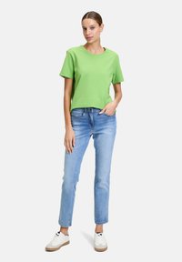 Zielona, teksturowana koszulka z krótkim rękawem w połączeniu z jasnoniebieskimi dżinsami prostymi oraz białymi sneakersami z beżowymi podeszwami. Prosty i casualowy strój.