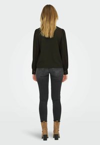 Zwarte blouse met lange mouwen en pofmouwen, gecombineerd met donkere grijze skinny jeans en tan enkellaarsjes met een blokhak. Achteraanzicht.