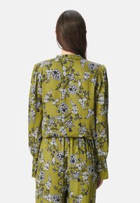 Grün gemusterte Bluse mit floralen Motiven und schwarz-weißen Akzenten, langen Ärmeln und taillierter Passform. Glattes Gewebe mit einem Kragenrücken-Design.