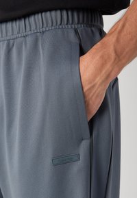 Pantalones jogger grises, texturizados, con una cintura elástica. Presentan bolsillos laterales y una etiqueta con el logo de Calvin Klein en el muslo izquierdo.