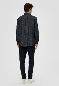 Marineblauw textuur shirt met een rugplooi, lange mouwen en knoopmanchetten; gecombineerd met donkere broek en crèmekleurige sneakers.