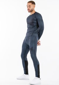 Súprava s dlhým rukávom, pozostávajúca z atletickej košele a legín, vyrobená z texturovanej šedej tkaniny s čiernymi akcentmi, s jemným logom a priliehavým strihom.