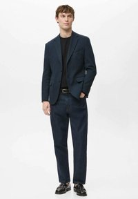 Marineblauw colbert met een subtiele structuur, een eenrijgig ontwerp, twee steekzakken aan de voorkant, gecombineerd met donkere denim broek en zwarte formele schoenen.