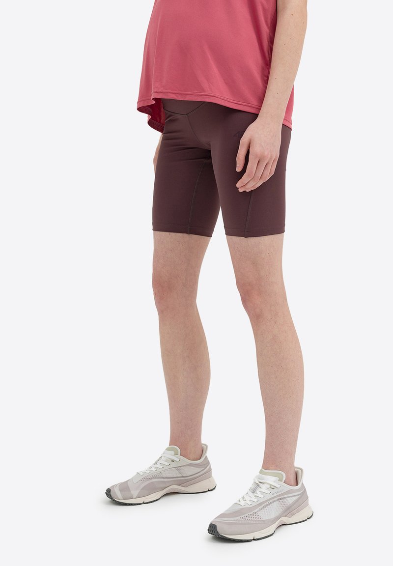 Shorts sportivi color bordeaux con texture liscia, taglio aderente e cuciture in contrasto, abbinati a scarpe da corsa grigio chiaro con dettagli in mesh.