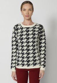 Pulover cu model houndstooth alb și negru, cu o textură pufoasă, guler rotund și manșete ribbate, asortat cu pantaloni bordeaux.