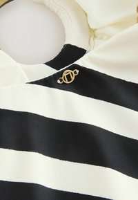 Tissu rayé noir et blanc avec une texture lisse, présentant un col rond et un accent en métal doré.