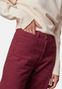 Bordeauxkleurige corduroy broek met verticale ribbeltextuur, hoge taille en voorzakken, gecombineerd met een romige lange mouw top.