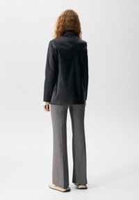 Blazer de cuero negro con ajuste entallado y cuello con muesca, combinado con pantalones grises acampanados. Los zapatos son de color claro con suela texturizada.