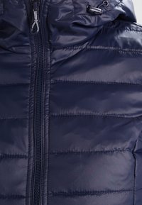 Chaqueta acolchada azul marino con cremallera frontal, capucha con cordón y textura acolchada para aislamiento.