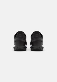 Svarta sportskor med ett texturerat tygöverdel, vit mellansula och svart gummisula. Har dragflikar vid hälen för enkel påklädning.