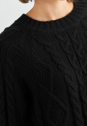 Pull noir en tricot torsadé avec un col rond côtelé et des motifs texturés, doté d'une finition en tricot épaisse et douce.