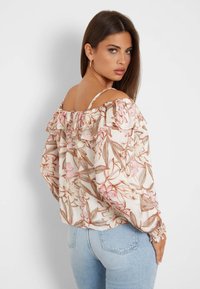 Cvjetna bluza bez ramena u svijetloj bež boji s ružičastim i smeškim uzorcima. Ima volane na rubovima i dugačke, napuhane rukave s elastičnim manžetama.