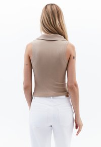 Top senza maniche a coste beige con colletto, abbinato a pantaloni bianchi a vita alta con tasche posteriori. Tessuto liscio, design aderente.