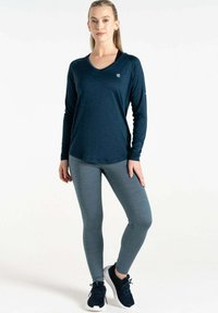 Dunkelblaues langärmliges Sportoberteil mit V-Ausschnitt, kombiniert mit leggings in schiefergrau. Beide Stoffe haben feine Texturen und werden mit schwarzen Sportschuhen getragen.