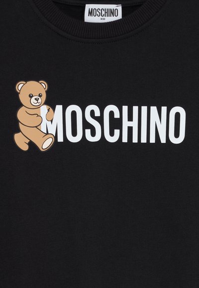 T-shirt noir Moschino Kid avec texte logo blanc et un graphique d'ours en peluche marron tenant la première lettre "M" du logo.