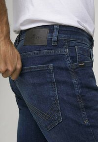 Jeans de denim en azul oscuro, con un parche de marca de cuero en la parte posterior, costuras en contraste y un diseño ajustado con cinco bolsillos.