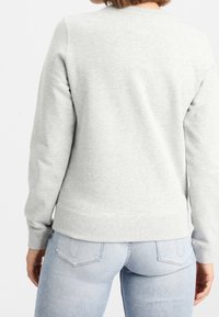 Sudadera gris claro con cuello redondo y puños de canalé, hecha de una tela suave. Textura suave y diseño ajustado.