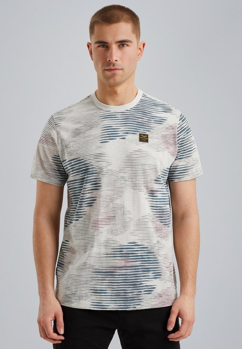 T-shirt à manches courtes en coton avec une base crème, présentant des motifs de vagues bleues et rouges, et un petit écusson logo sur la poitrine.