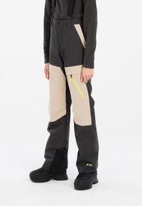 Pantalons de ski noirs et beiges, dotés de bretelles ajustables, de poches latérales zippées avec des accents néon et d'une texture imperméable.