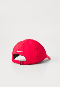Casquette de baseball en tissu rouge avec une visière incurvée, arborant un logo Nike en swoosh blanc à l'arrière et une fermeture réglable.