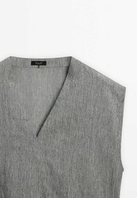 Haut gris sans manches en tissu texturé avec col en V et étiquette de marque visible à l'intérieur du col sur fond blanc.