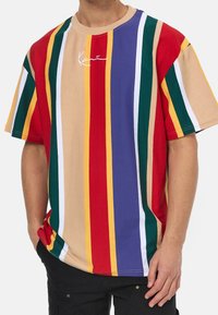 Camiseta de gran tamaño multicolor con rayas verticales en rojo, verde, amarillo, púrpura y beige. Presenta un cuello redondo y un logotipo en el frontal.