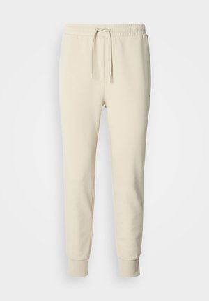 Svetlosmeđe trenirka s trakicom za stezanje u struku, suženim nogavicama i rebrastim manžetama. Izrađene od mekanog, teksturiranog tkanja. Bez uzoraka ili naglasaka.