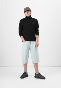 Col roulé noir, shorts en denim bleu clair, casquette à carreaux et baskets noires. Les accessoires incluent des chaussettes grises ; tenue décontractée avec une silhouette relaxée.