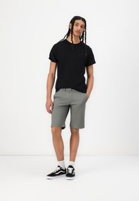 Black cotton t-shirt with short sleeves and a small logo, paired with gray knee-length shorts and black sneakers with white soles and laces.