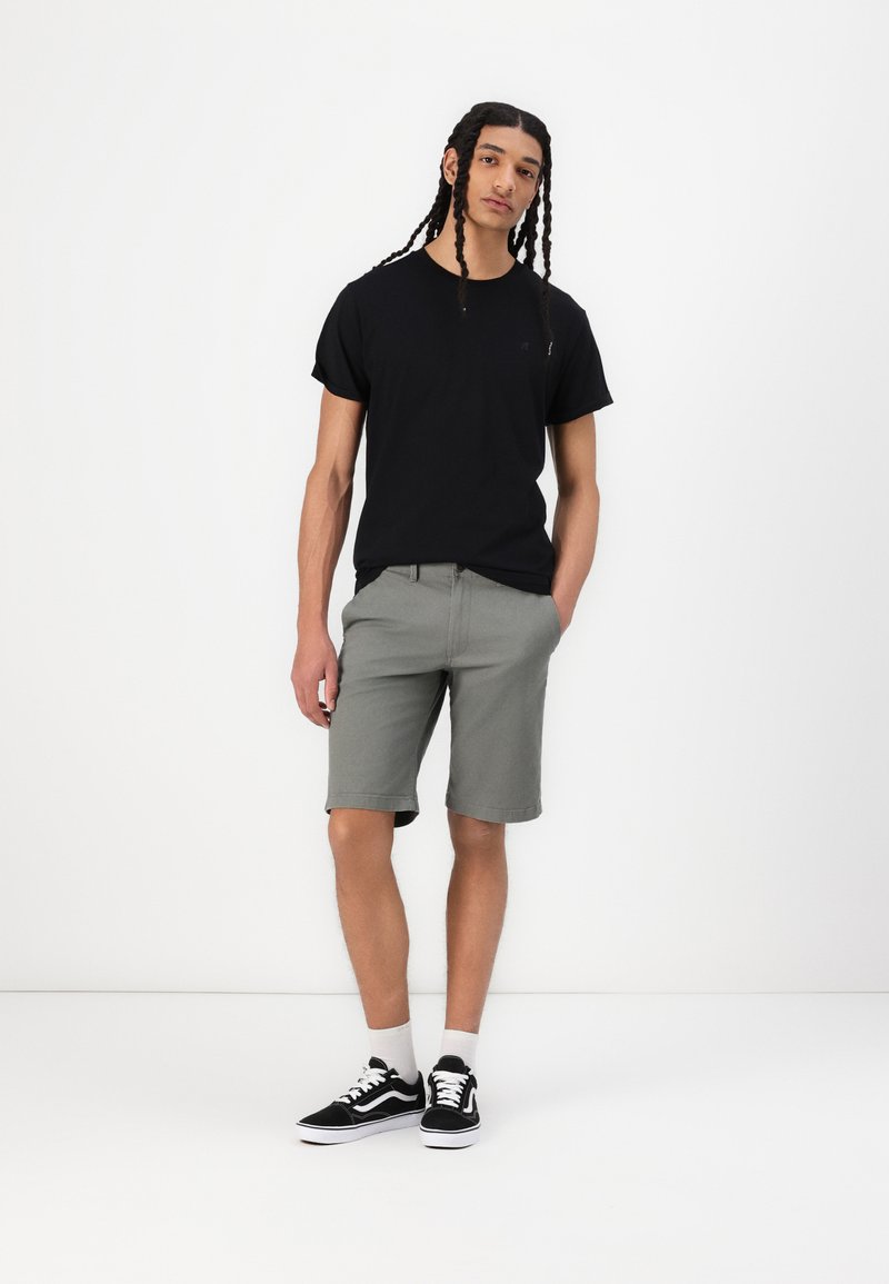 Black cotton t-shirt with short sleeves and a small logo, paired with gray knee-length shorts and black sneakers with white soles and laces.