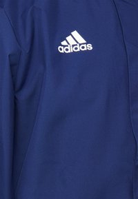 Blått tyg med vitt Adidas-logotyp som har tre diagonala ränder och "adidas" text i gemener.