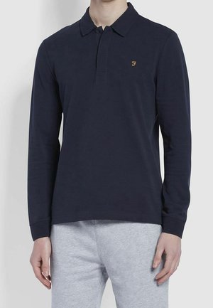 Polo à manches longues bleu marine avec un plastron à trois boutons et un logo brodé en or sur la poitrine gauche. Tissu lisse, coupe classique.