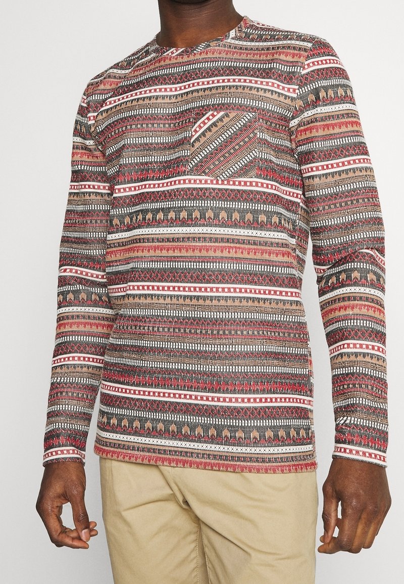 Camicia a maniche lunghe con un motivo etnico multicolore, caratterizzata da design geometrici in rosso, beige e nero, e una tasca sul petto. Materiale in cotone.